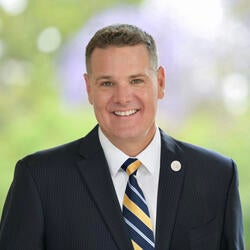 Jeff Girod, Assistant Dean of Marketing and Communications at UC Riverside, wearing a yellow and blue tie with a black striped suit coat, smiling for headshot 