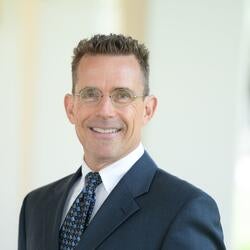 Aaron Bushong, Administrative Director, University Honors at UC Riverside, wearing a blue suit with a tie smiling for headshot