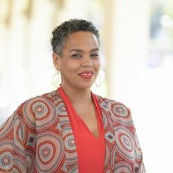 Rochelle Settle, Financial & Administrative Assistant at UC Riverside, wearing a orange shirt with circular design throw that has shades of orange and light blue,, smiling for a headshot