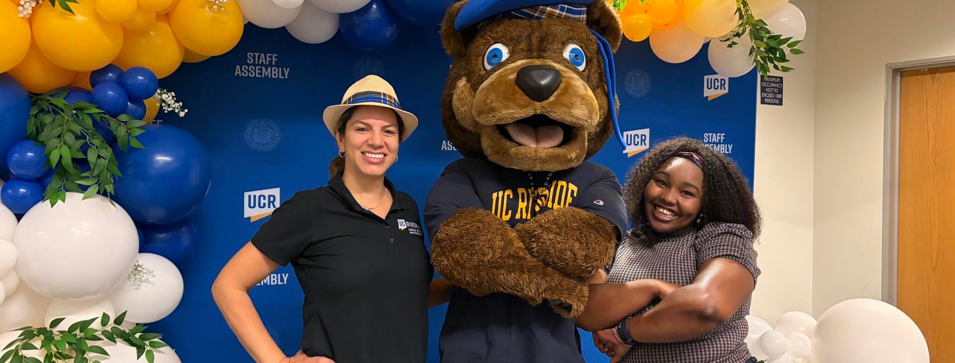 Two UCR staff members posing with Scotty Bear in front of the balloon arch photo booth.